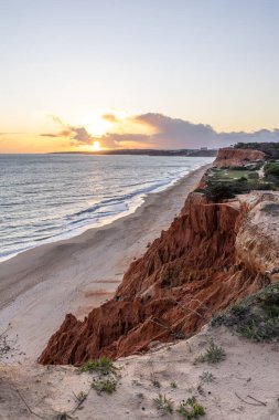 Atlantik Okyanusu 'nda çarpıcı oluşumları olan kayalıklar. Manzara çekiminde sıcak gün batımı. Sahilde ve denizde çarpıcı oluşumlara sahip kızıl kayalıklar, Praia da Falsia, Algarve, Portekiz