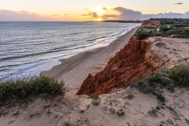 Atlantik Okyanusu 'nda çarpıcı oluşumları olan kayalıklar. Manzara çekiminde sıcak gün batımı. Sahilde ve denizde çarpıcı oluşumlara sahip kızıl kayalıklar, Praia da Falsia, Algarve, Portekiz