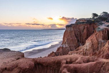 Atlantik Okyanusu 'nda çarpıcı oluşumları olan kayalıklar. Manzara çekiminde sıcak gün batımı. Sahilde ve denizde çarpıcı oluşumlara sahip kızıl kayalıklar, Praia da Falsia, Algarve, Portekiz