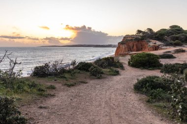 Atlantik Okyanusu 'nda çarpıcı oluşumları olan kayalıklar. Manzara çekiminde sıcak gün batımı. Sahilde ve denizde çarpıcı oluşumlara sahip kızıl kayalıklar, Praia da Falsia, Algarve, Portekiz