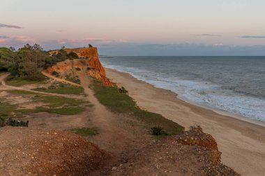 Atlantik Okyanusu 'nda çarpıcı oluşumları olan kayalıklar. Manzara çekiminde sıcak gün batımı. Sahilde ve denizde çarpıcı oluşumlara sahip kızıl kayalıklar, Praia da Falsia, Algarve, Portekiz