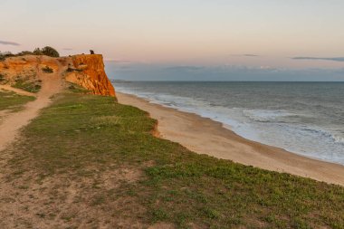 Atlantik Okyanusu 'nda çarpıcı oluşumları olan kayalıklar. Manzara çekiminde sıcak gün batımı. Sahilde ve denizde çarpıcı oluşumlara sahip kızıl kayalıklar, Praia da Falsia, Algarve, Portekiz