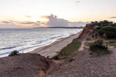 Atlantik Okyanusu 'nda çarpıcı oluşumları olan kayalıklar. Manzara çekiminde sıcak gün batımı. Sahilde ve denizde çarpıcı oluşumlara sahip kızıl kayalıklar, Praia da Falsia, Algarve, Portekiz