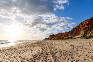 Okyanus kıyısında inanılmaz bir kaya oluşumu. Kızıl toprağı ve geniş kumsalda çarpıcı oluşumları olan kızıl kayalıklar. Praia da Falsia, güneş batarken sıcak bir ışıkta yıkandı, Algarve, Portekiz