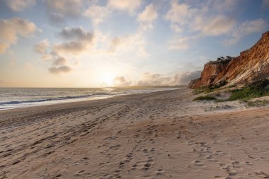 Okyanus kıyısında inanılmaz bir kaya oluşumu. Kızıl toprağı ve geniş kumsalda çarpıcı oluşumları olan kızıl kayalıklar. Praia da Falsia, güneş batarken sıcak bir ışıkta yıkandı, Algarve, Portekiz