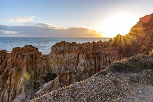 Atlantik Okyanusu 'nda çarpıcı oluşumları olan kayalıklar. Manzara çekiminde sıcak gün batımı. Sahilde ve denizde çarpıcı oluşumlara sahip kızıl kayalıklar, Praia da Falsia, Algarve, Portekiz