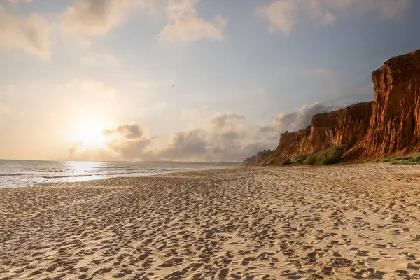 Okyanus kıyısında inanılmaz bir kaya oluşumu. Kızıl toprağı ve geniş kumsalda çarpıcı oluşumları olan kızıl kayalıklar. Praia da Falsia, güneş batarken sıcak bir ışıkta yıkandı, Algarve, Portekiz