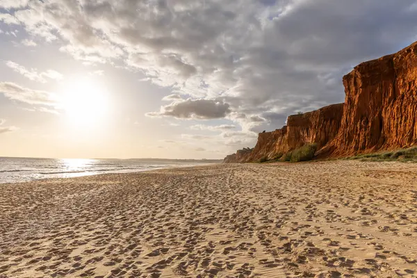 Okyanus kıyısında inanılmaz bir kaya oluşumu. Kızıl toprağı ve geniş kumsalda çarpıcı oluşumları olan kızıl kayalıklar. Praia da Falsia, güneş batarken sıcak bir ışıkta yıkandı, Algarve, Portekiz
