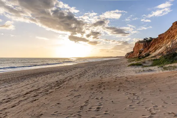 Okyanus kıyısında inanılmaz bir kaya oluşumu. Kızıl toprağı ve geniş kumsalda çarpıcı oluşumları olan kızıl kayalıklar. Praia da Falsia, güneş batarken sıcak bir ışıkta yıkandı, Algarve, Portekiz