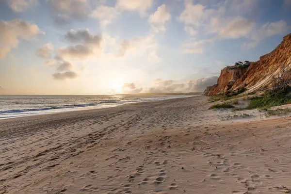 Okyanus kıyısında inanılmaz bir kaya oluşumu. Kızıl toprağı ve geniş kumsalda çarpıcı oluşumları olan kızıl kayalıklar. Praia da Falsia, güneş batarken sıcak bir ışıkta yıkandı, Algarve, Portekiz
