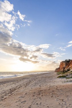 Okyanus kıyısında inanılmaz bir kaya oluşumu. Kızıl toprağı ve geniş kumsalda çarpıcı oluşumları olan kızıl kayalıklar. Praia da Falsia, güneş batarken sıcak bir ışıkta yıkandı, Algarve, Portekiz