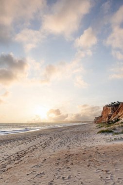 Okyanus kıyısında inanılmaz bir kaya oluşumu. Kızıl toprağı ve geniş kumsalda çarpıcı oluşumları olan kızıl kayalıklar. Praia da Falsia, güneş batarken sıcak bir ışıkta yıkandı, Algarve, Portekiz