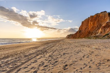 Okyanus kıyısında inanılmaz bir kaya oluşumu. Kızıl toprağı ve geniş kumsalda çarpıcı oluşumları olan kızıl kayalıklar. Praia da Falsia, güneş batarken sıcak bir ışıkta yıkandı, Algarve, Portekiz