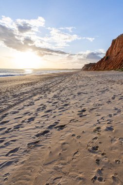 Okyanus kıyısında inanılmaz bir kaya oluşumu. Kızıl toprağı ve geniş kumsalda çarpıcı oluşumları olan kızıl kayalıklar. Praia da Falsia, güneş batarken sıcak bir ışıkta yıkandı, Algarve, Portekiz