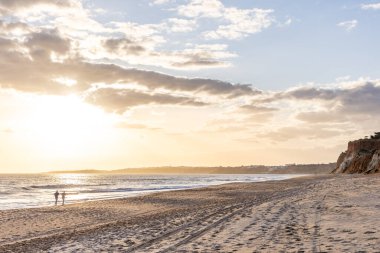 Okyanus kıyısında inanılmaz bir kaya oluşumu. Kızıl toprağı ve geniş kumsalda çarpıcı oluşumları olan kızıl kayalıklar. Praia da Falsia, güneş batarken sıcak bir ışıkta yıkandı, Algarve, Portekiz