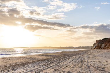 Okyanus kıyısında inanılmaz bir kaya oluşumu. Kızıl toprağı ve geniş kumsalda çarpıcı oluşumları olan kızıl kayalıklar. Praia da Falsia, güneş batarken sıcak bir ışıkta yıkandı, Algarve, Portekiz