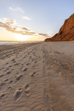 Okyanus kıyısında inanılmaz bir kaya oluşumu. Kızıl toprağı ve geniş kumsalda çarpıcı oluşumları olan kızıl kayalıklar. Praia da Falsia, güneş batarken sıcak bir ışıkta yıkandı, Algarve, Portekiz
