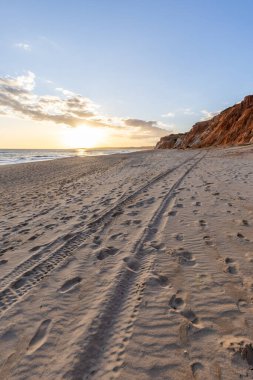 Okyanus kıyısında inanılmaz bir kaya oluşumu. Kızıl toprağı ve geniş kumsalda çarpıcı oluşumları olan kızıl kayalıklar. Praia da Falsia, güneş batarken sıcak bir ışıkta yıkandı, Algarve, Portekiz