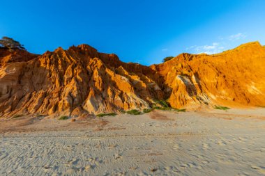 Bir çakıl taşı ve kumsalda inanılmaz kaya oluşumu. Kızıl topraklı kızıl kayalıklar ve kumlu sahilde inanılmaz oluşumlar. Praia da Falsia, sıcak güneş ışığıyla yıkanmış, Algarve, Portekiz