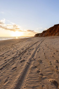 Okyanus kıyısında inanılmaz bir kaya oluşumu. Kızıl toprağı ve geniş kumsalda çarpıcı oluşumları olan kızıl kayalıklar. Praia da Falsia, güneş batarken sıcak bir ışıkta yıkandı, Algarve, Portekiz