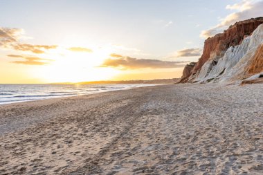 Okyanus kıyısında inanılmaz bir kaya oluşumu. Kızıl toprağı ve geniş kumsalda çarpıcı oluşumları olan kızıl kayalıklar. Praia da Falsia, güneş batarken sıcak bir ışıkta yıkandı, Algarve, Portekiz
