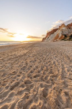 Okyanus kıyısında inanılmaz bir kaya oluşumu. Kızıl toprağı ve geniş kumsalda çarpıcı oluşumları olan kızıl kayalıklar. Praia da Falsia, güneş batarken sıcak bir ışıkta yıkandı, Algarve, Portekiz