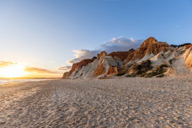 Okyanus kıyısında inanılmaz bir kaya oluşumu. Kızıl toprağı ve geniş kumsalda çarpıcı oluşumları olan kızıl kayalıklar. Praia da Falsia, güneş batarken sıcak bir ışıkta yıkandı, Algarve, Portekiz