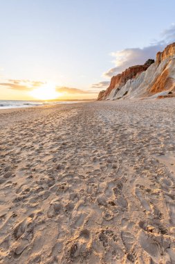 Okyanus kıyısında inanılmaz bir kaya oluşumu. Kızıl toprağı ve geniş kumsalda çarpıcı oluşumları olan kızıl kayalıklar. Praia da Falsia, güneş batarken sıcak bir ışıkta yıkandı, Algarve, Portekiz