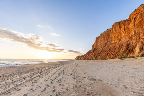 Okyanus kıyısında inanılmaz bir kaya oluşumu. Kızıl toprağı ve geniş kumsalda çarpıcı oluşumları olan kızıl kayalıklar. Praia da Falsia, güneş batarken sıcak bir ışıkta yıkandı, Algarve, Portekiz