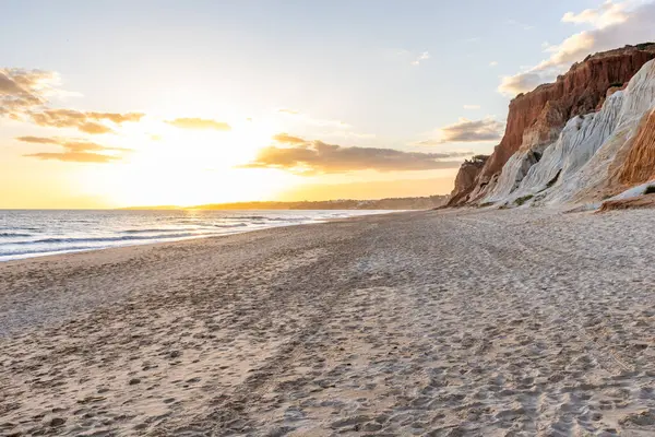 Okyanus kıyısında inanılmaz bir kaya oluşumu. Kızıl toprağı ve geniş kumsalda çarpıcı oluşumları olan kızıl kayalıklar. Praia da Falsia, güneş batarken sıcak bir ışıkta yıkandı, Algarve, Portekiz