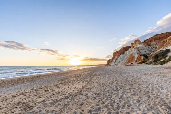Okyanus kıyısında inanılmaz bir kaya oluşumu. Kızıl toprağı ve geniş kumsalda çarpıcı oluşumları olan kızıl kayalıklar. Praia da Falsia, güneş batarken sıcak bir ışıkta yıkandı, Algarve, Portekiz