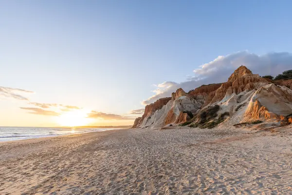 Okyanus kıyısında inanılmaz bir kaya oluşumu. Kızıl toprağı ve geniş kumsalda çarpıcı oluşumları olan kızıl kayalıklar. Praia da Falsia, güneş batarken sıcak bir ışıkta yıkandı, Algarve, Portekiz