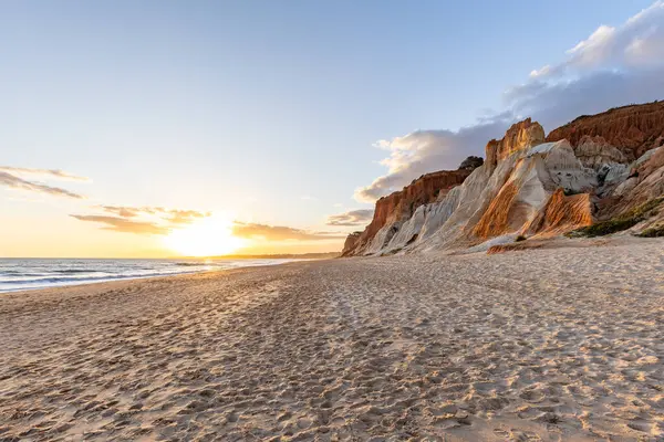 Okyanus kıyısında inanılmaz bir kaya oluşumu. Kızıl toprağı ve geniş kumsalda çarpıcı oluşumları olan kızıl kayalıklar. Praia da Falsia, güneş batarken sıcak bir ışıkta yıkandı, Algarve, Portekiz