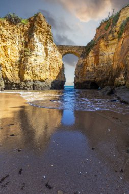 Kumsaldaki sarı kayalar ve uçurumlar. Eski Pinhao Fort Köprüsü 'nün iki uçurumu birleştirdiği deniz kenarında bir koy. Praia da Caldeira plajı, Lagos. Algarve, Portekiz