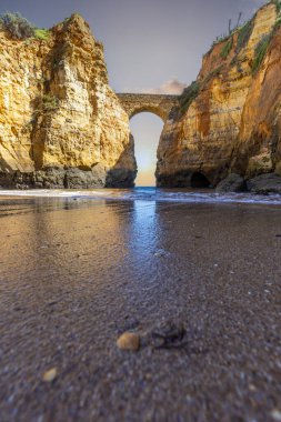 Kumsaldaki sarı kayalar ve uçurumlar. Eski Pinhao Fort Köprüsü 'nün iki uçurumu birleştirdiği deniz kenarında bir koy. Praia da Caldeira plajı, Lagos. Algarve, Portekiz