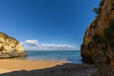 Kumsaldaki sarı kayalar ve uçurumlar. Eski Pinhao Fort Köprüsü 'nün iki uçurumu birleştirdiği deniz kenarında bir koy. Praia da Caldeira plajı, Lagos. Algarve, Portekiz