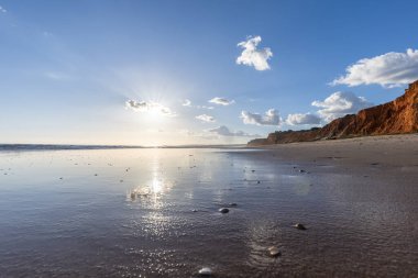 Praia da Falsia 'nın altın kumlu plajı, gökyüzünün yansıması ile kristal berraklığında deniz suyu, batan güneş, ve karakteristik turuncu kayalıklar, Algarve, Portekiz
