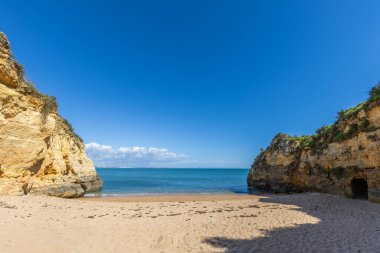 Kumsaldaki sarı kayalar ve uçurumlar. Eski Pinhao Fort Köprüsü 'nün iki uçurumu birleştirdiği deniz kenarında bir koy. Praia da Caldeira plajı, Lagos. Algarve, Portekiz