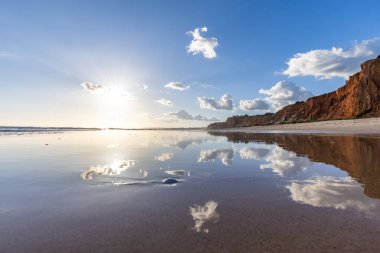 Praia da Falsia 'nın altın kumlu plajı, gökyüzünün yansıması ile kristal berraklığında deniz suyu, batan güneş, ve karakteristik turuncu kayalıklar, Algarve, Portekiz