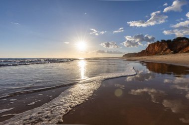 Praia da Falsia 'nın altın kumlu plajı, gökyüzünün yansıması ile kristal berraklığında deniz suyu, batan güneş, ve karakteristik turuncu kayalıklar, Algarve, Portekiz