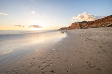 Praia da Falsia 'nın altın kumlu plajı, gökyüzünün yansıması ile kristal berraklığında deniz suyu, batan güneş, ve karakteristik turuncu kayalıklar, Algarve, Portekiz