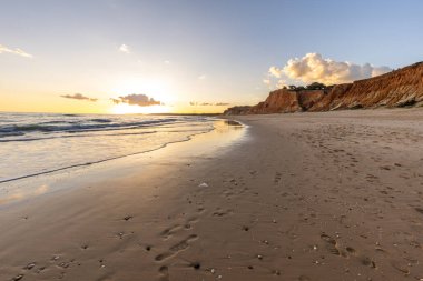 Praia da Falsia 'nın altın kumlu plajı, gökyüzünün yansıması ile kristal berraklığında deniz suyu, batan güneş, ve karakteristik turuncu kayalıklar, Algarve, Portekiz