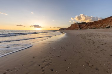 Praia da Falsia 'nın altın kumlu plajı, gökyüzünün yansıması ile kristal berraklığında deniz suyu, batan güneş, ve karakteristik turuncu kayalıklar, Algarve, Portekiz