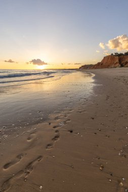 Praia da Falsia 'nın altın kumlu plajı, gökyüzünün yansıması ile kristal berraklığında deniz suyu, batan güneş, ve karakteristik turuncu kayalıklar, Algarve, Portekiz