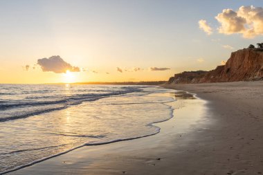 Praia da Falsia 'nın altın kumlu plajı, gökyüzünün yansıması ile kristal berraklığında deniz suyu, batan güneş, ve karakteristik turuncu kayalıklar, Algarve, Portekiz
