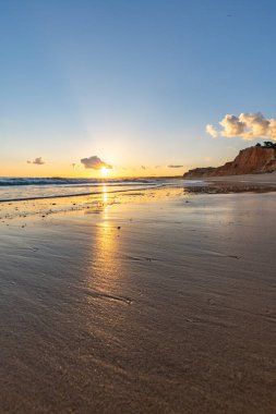 Praia da Falsia 'nın altın kumlu plajı, gökyüzünün yansıması ile kristal berraklığında deniz suyu, batan güneş, ve karakteristik turuncu kayalıklar, Algarve, Portekiz