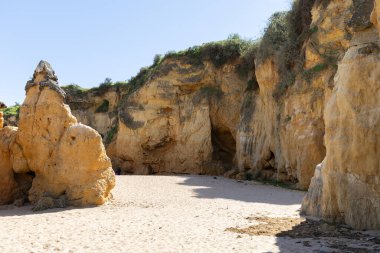 Kumsaldaki sarı kayalar ve uçurumlar. Eski Pinhao Fort Köprüsü 'nün iki uçurumu birleştirdiği deniz kenarında bir koy. Praia da Caldeira plajı, Lagos. Algarve, Portekiz