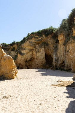 Kumsaldaki sarı kayalar ve uçurumlar. Eski Pinhao Fort Köprüsü 'nün iki uçurumu birleştirdiği deniz kenarında bir koy. Praia da Caldeira plajı, Lagos. Algarve, Portekiz