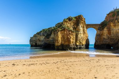 Kumsaldaki sarı kayalar ve uçurumlar. Eski Pinhao Fort Köprüsü 'nün iki uçurumu birleştirdiği deniz kenarında bir koy. Praia da Caldeira plajı, Lagos. Algarve, Portekiz