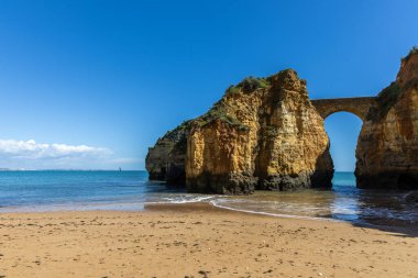 Kumsaldaki sarı kayalar ve uçurumlar. Eski Pinhao Fort Köprüsü 'nün iki uçurumu birleştirdiği deniz kenarında bir koy. Praia da Caldeira plajı, Lagos. Algarve, Portekiz